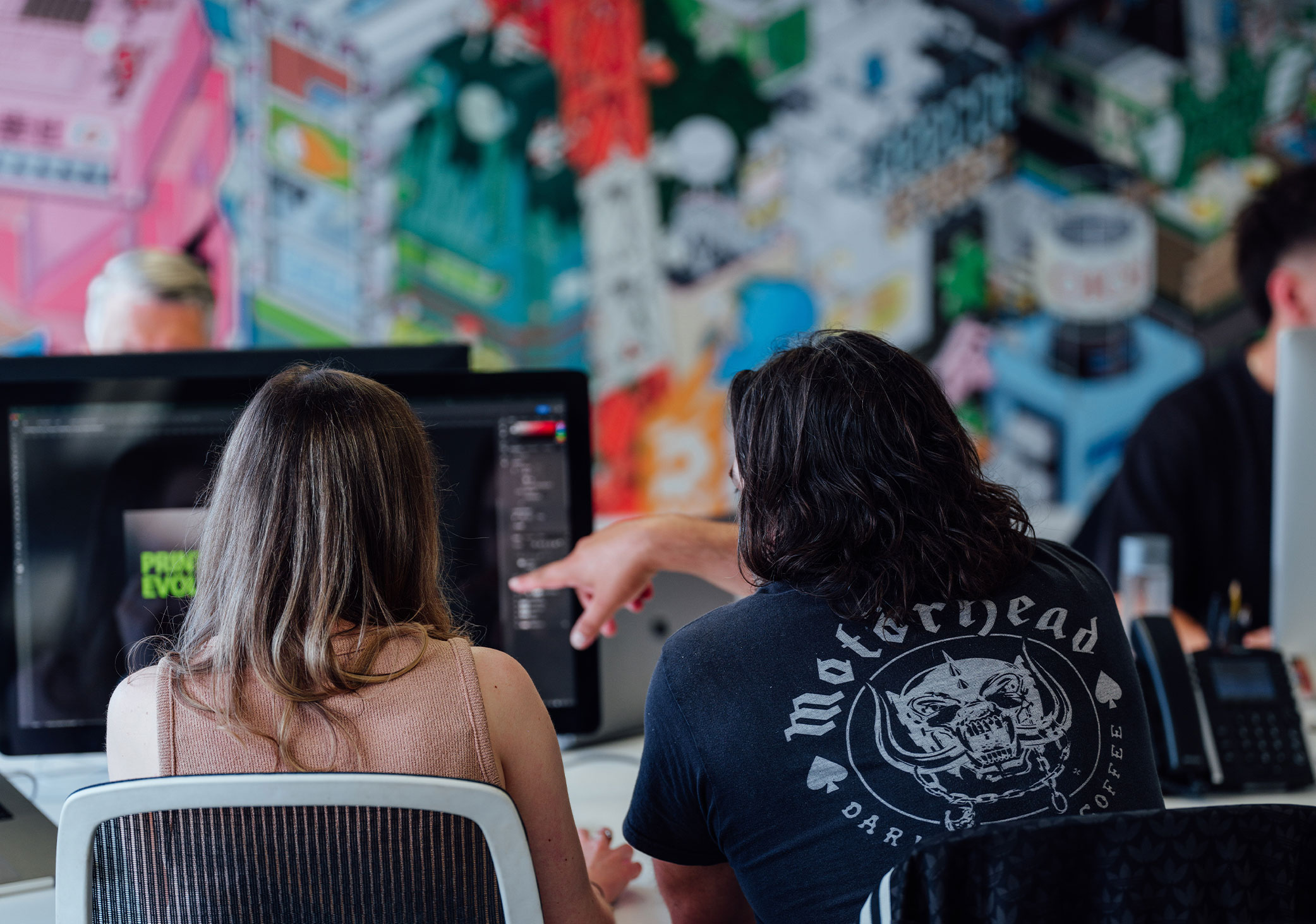 Image showing the back of two designers sat at a desk pointing at creative work on an iMac screen