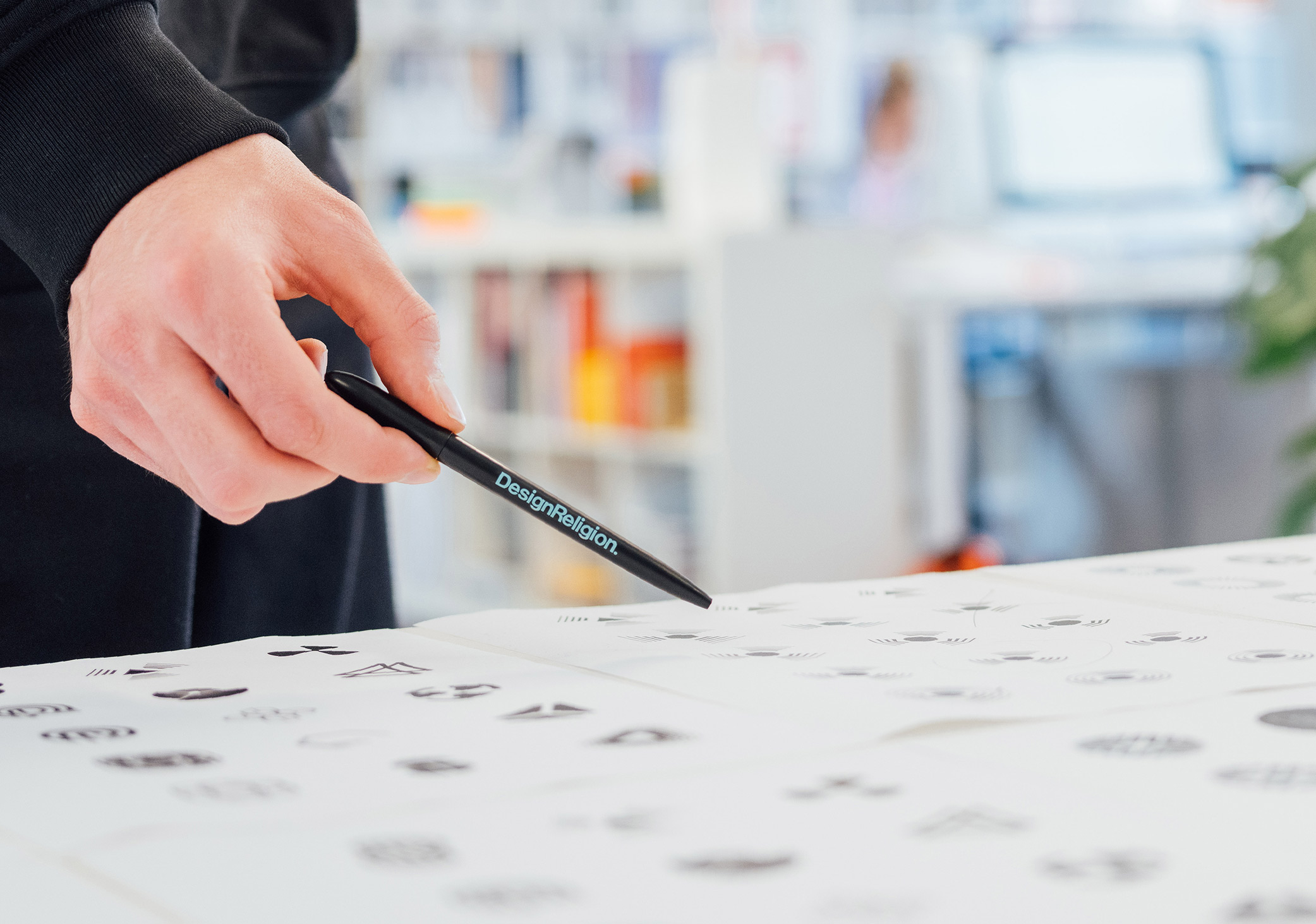 Close up photo of a hand holding a pen pointing at a design on a piece of paper